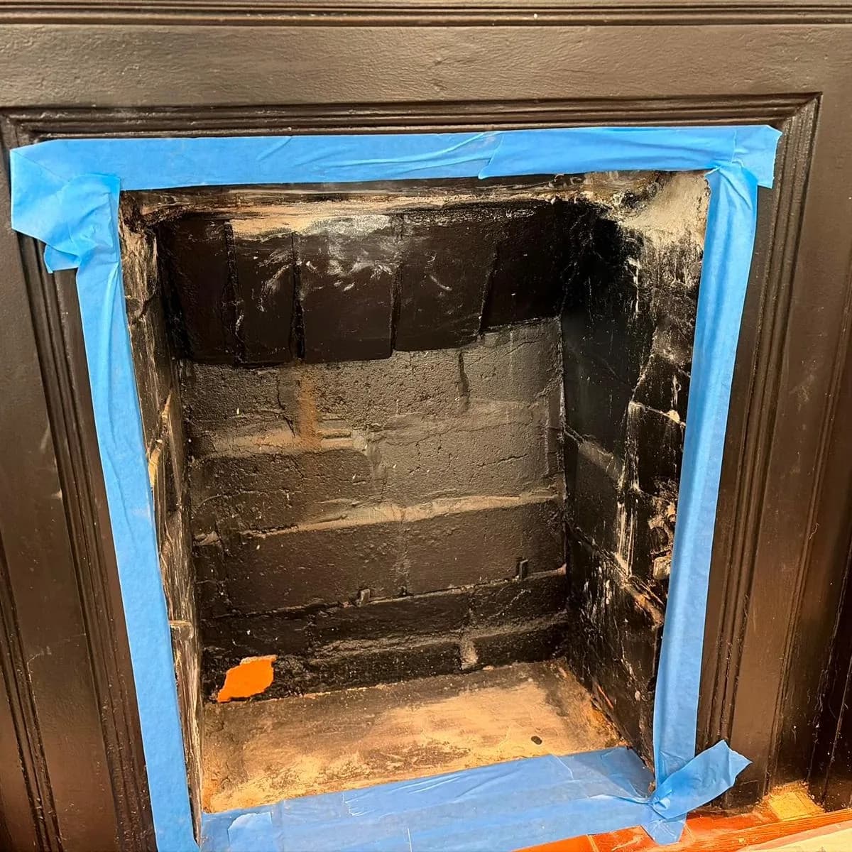 Before: A fireplace opening masked with painter's tape and its sooty firebrick exposed, and the same opening finished with a stove standing in it
