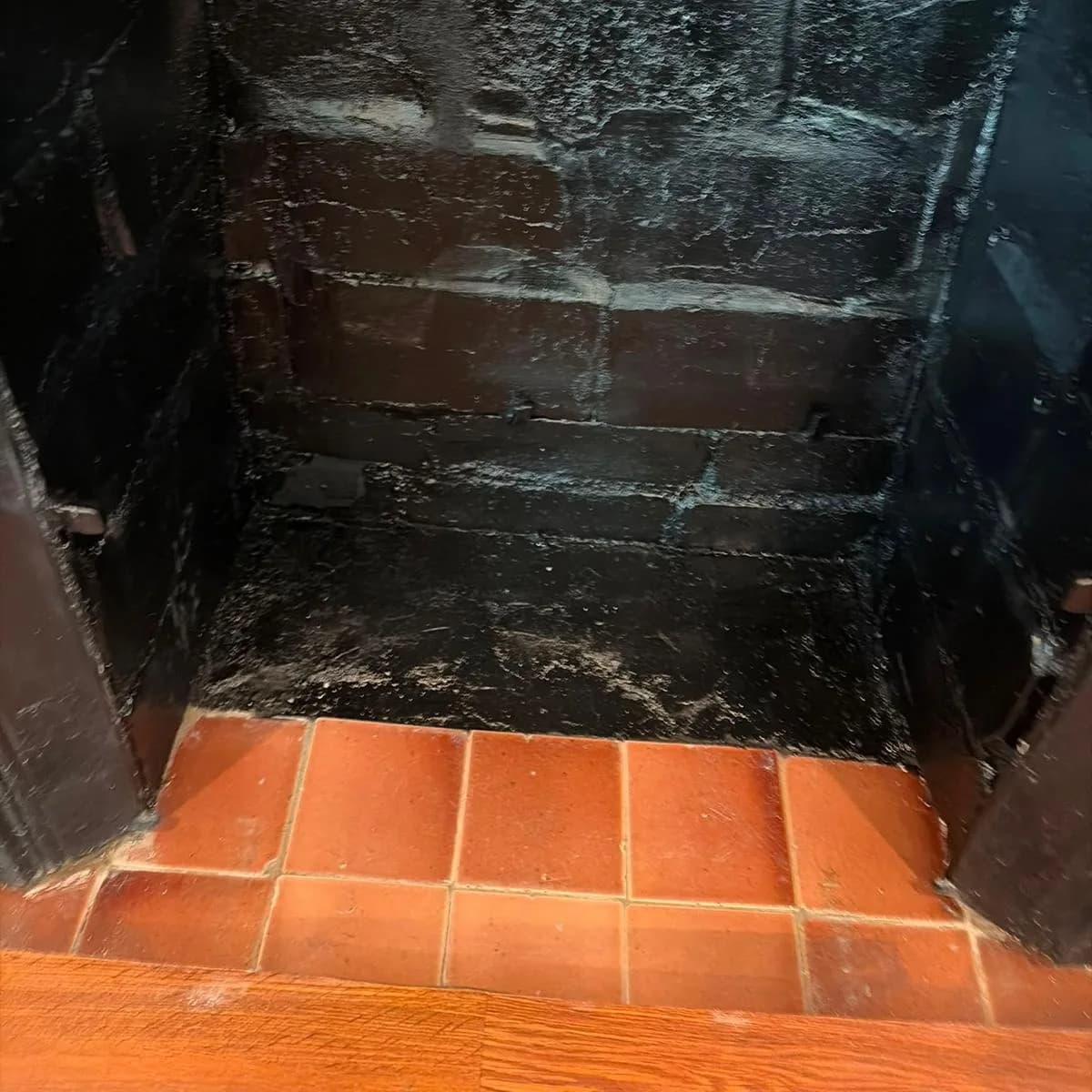 The inside of a swept firebox, black-coated brick above a clean terracotta tile hearth