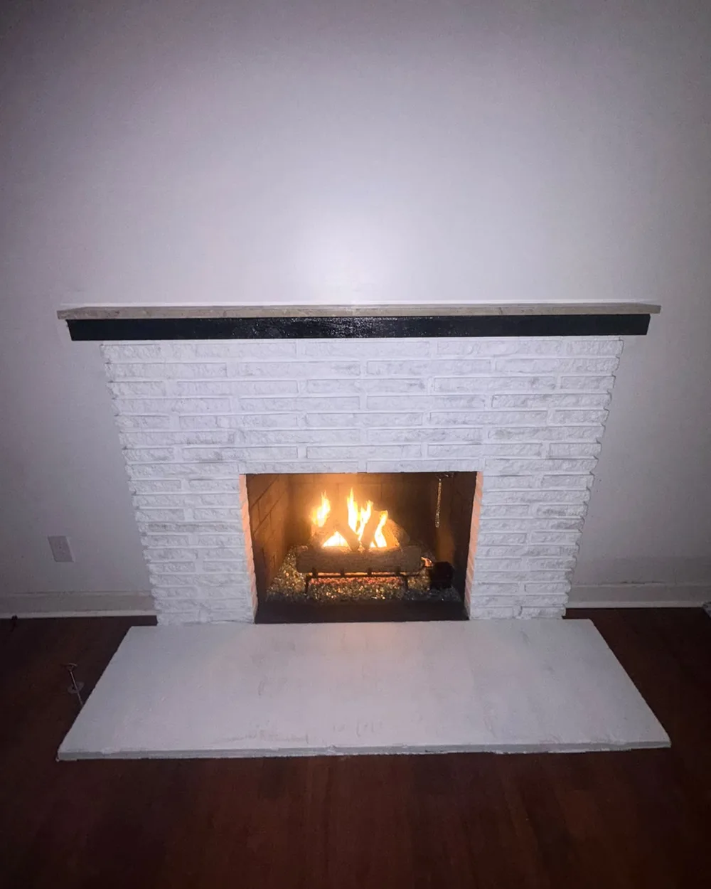 Wide view of the completed white brick fireplace with the fire lit