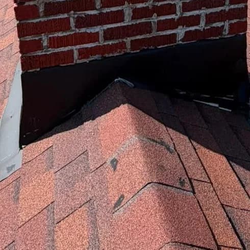 Chimney flashing sealed into the shingles where a roof ridge meets the brick stack