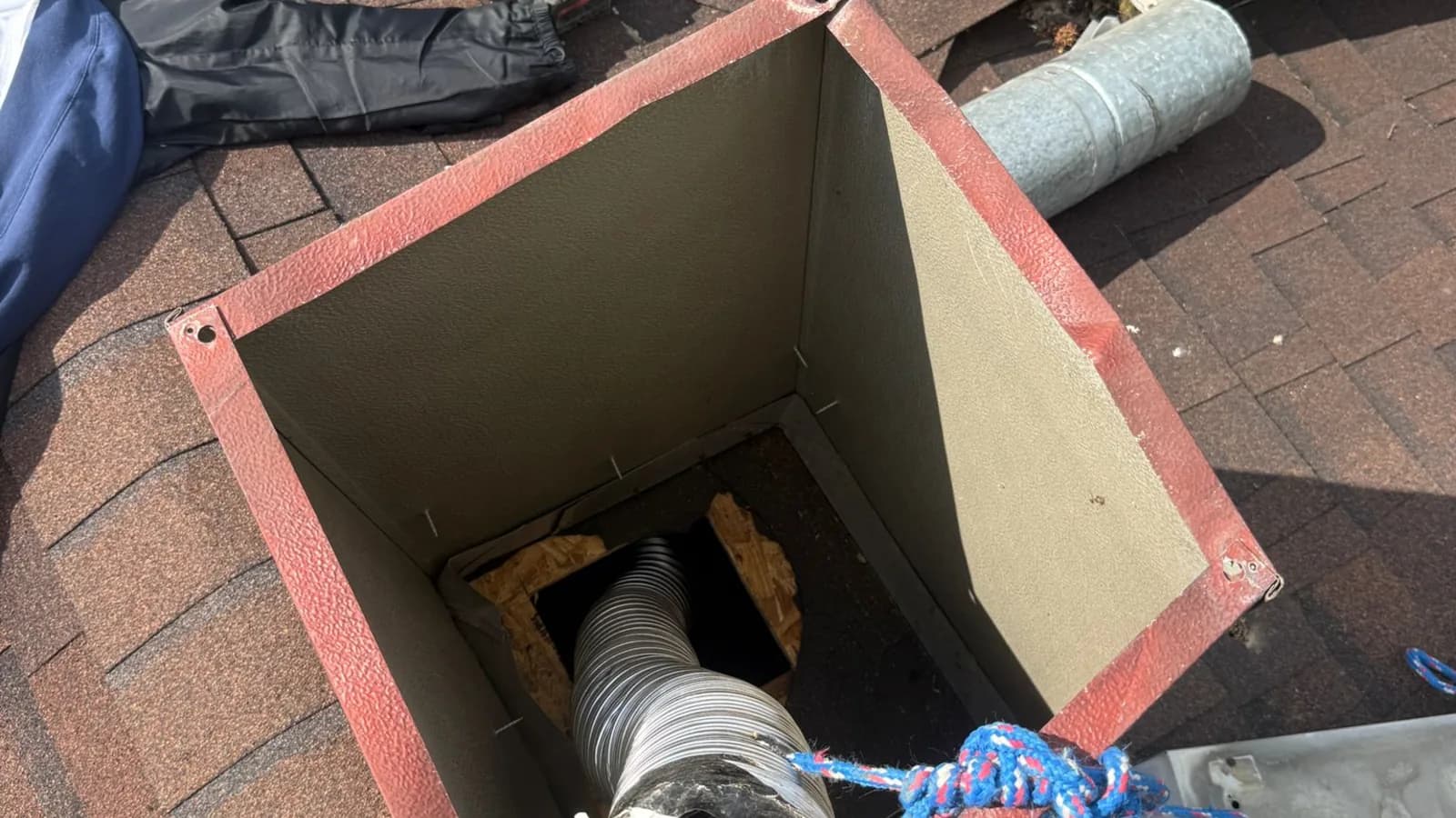 An opened chimney chase on a roof with a stainless flexible liner being fed down the flue