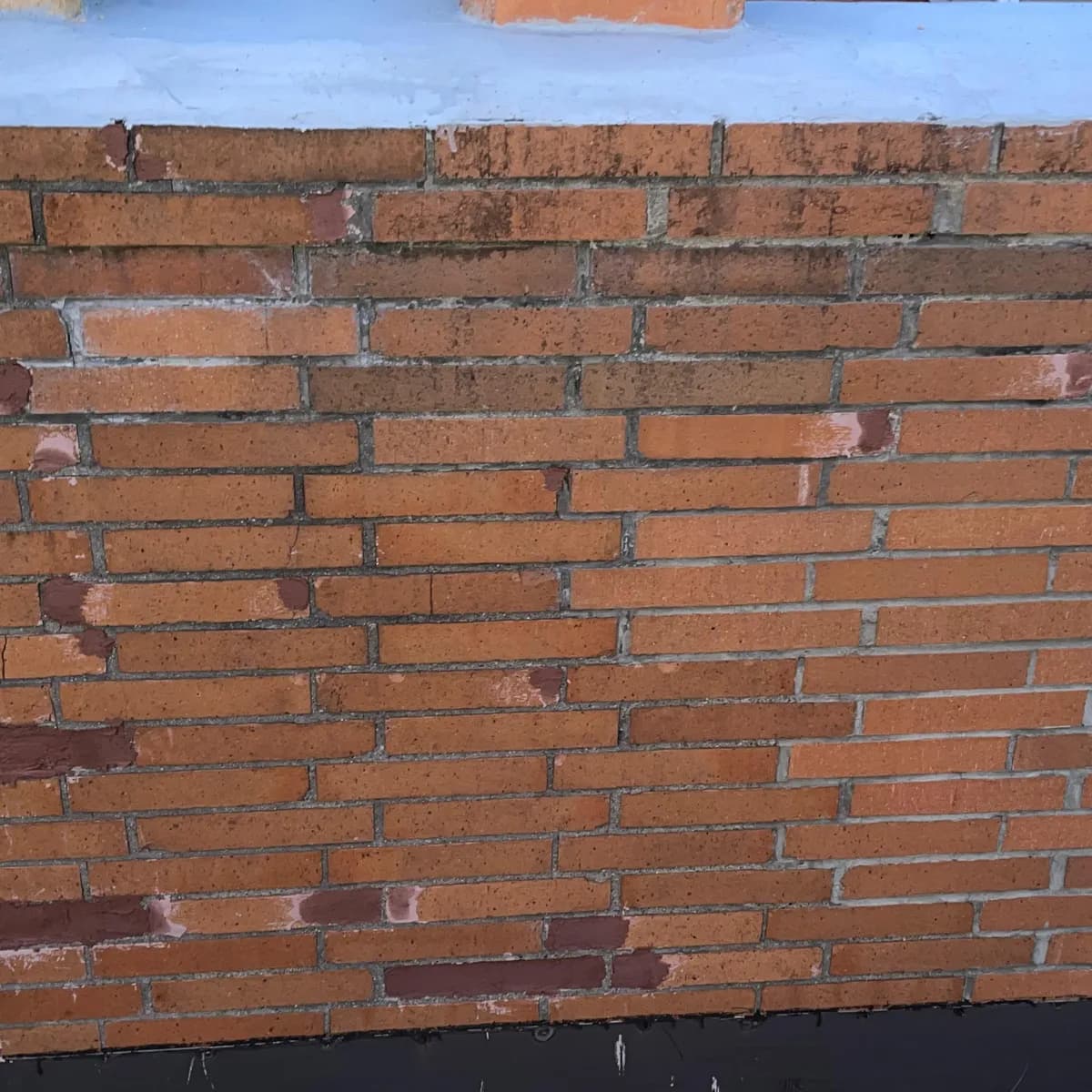 A broad brick chimney face with multiple repaired bricks and mortar joints beneath a light-colored crown