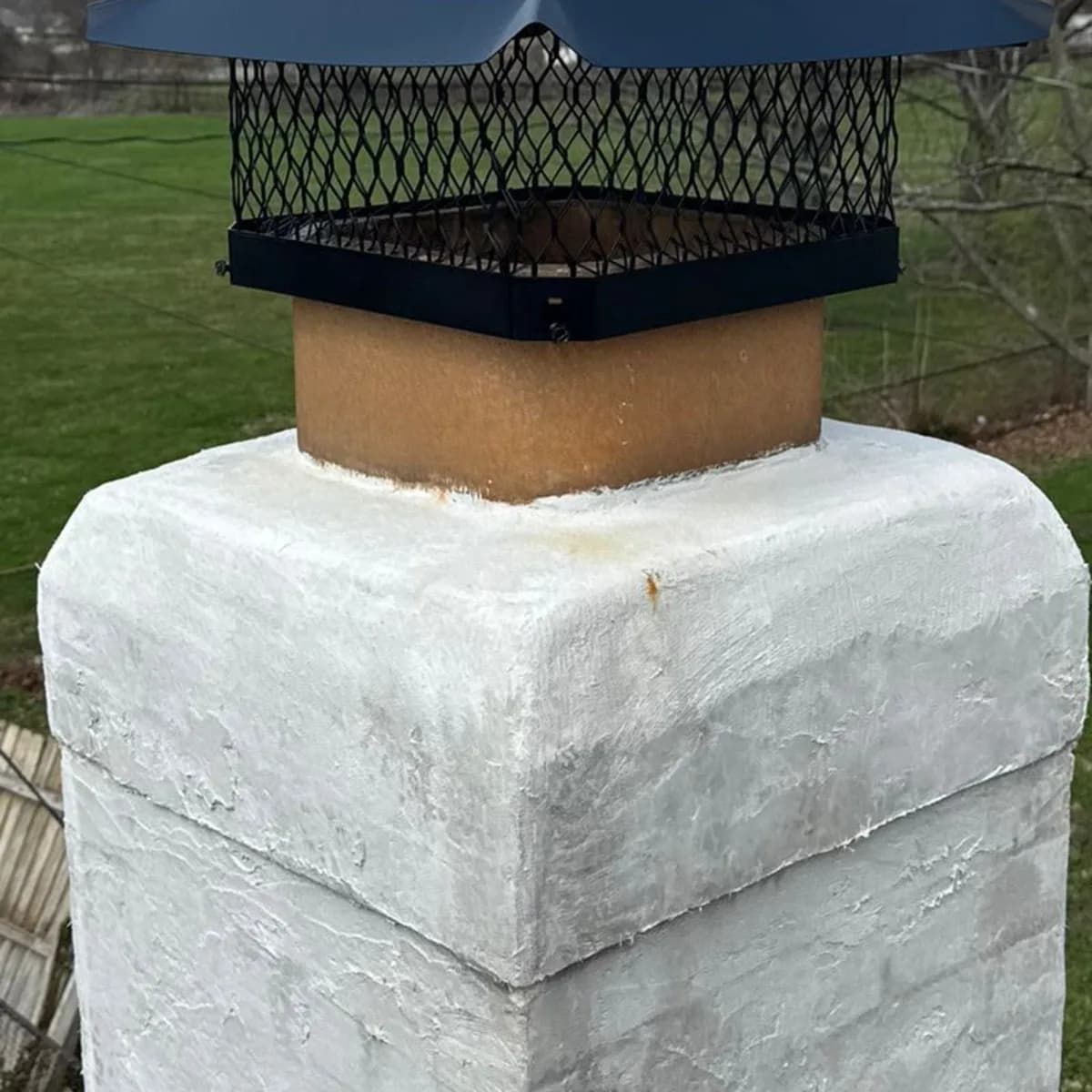A black screened metal chimney cap fitted over a flue on a light-colored chimney top