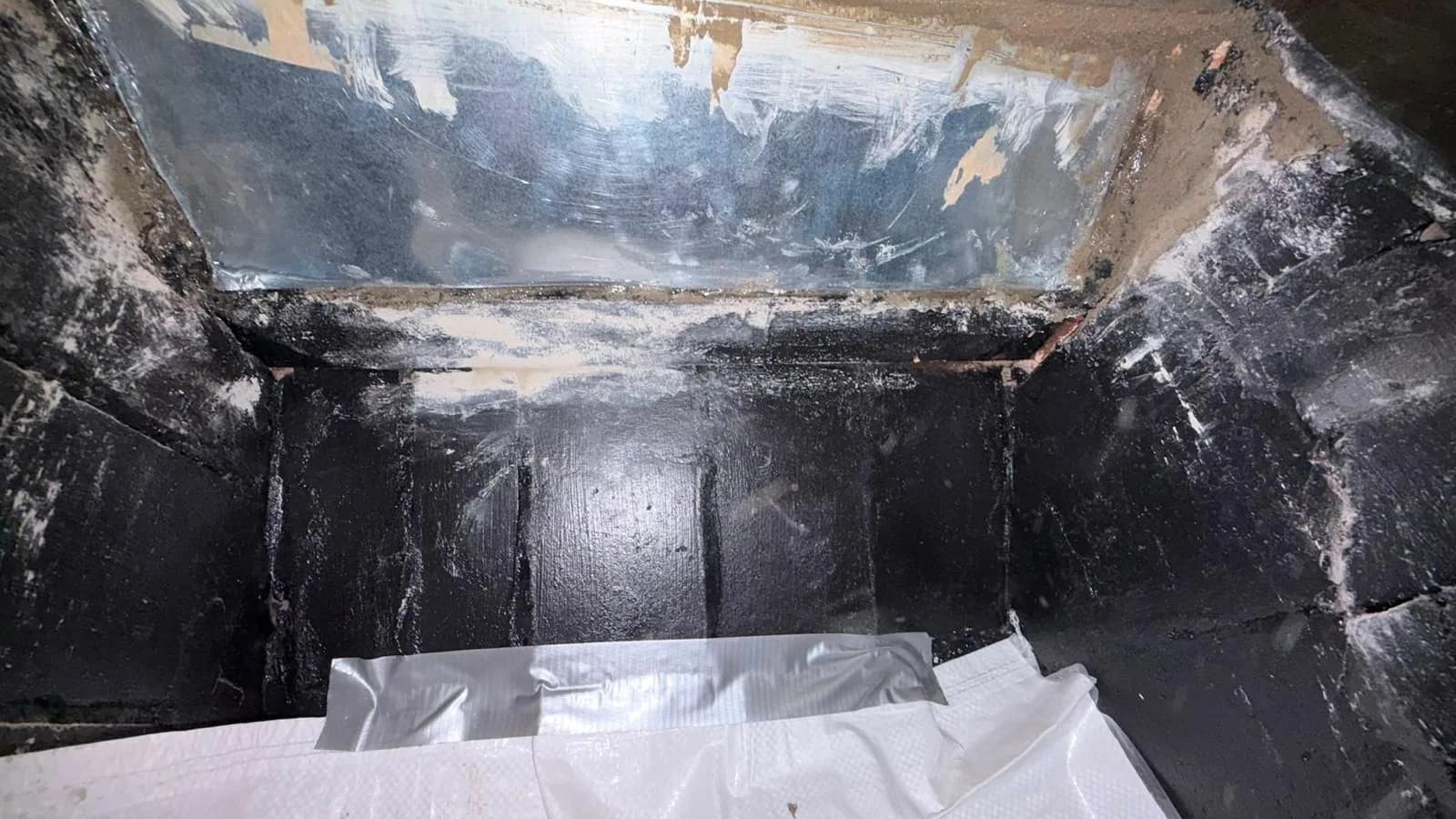 Looking up into a chimney smoke chamber with the sloping face freshly parged smooth above black-coated brick